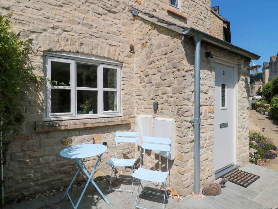 A stone house exterior with a white door number 2 and a small blue table with two blue chairs outside at Batemans in Nailsworth
