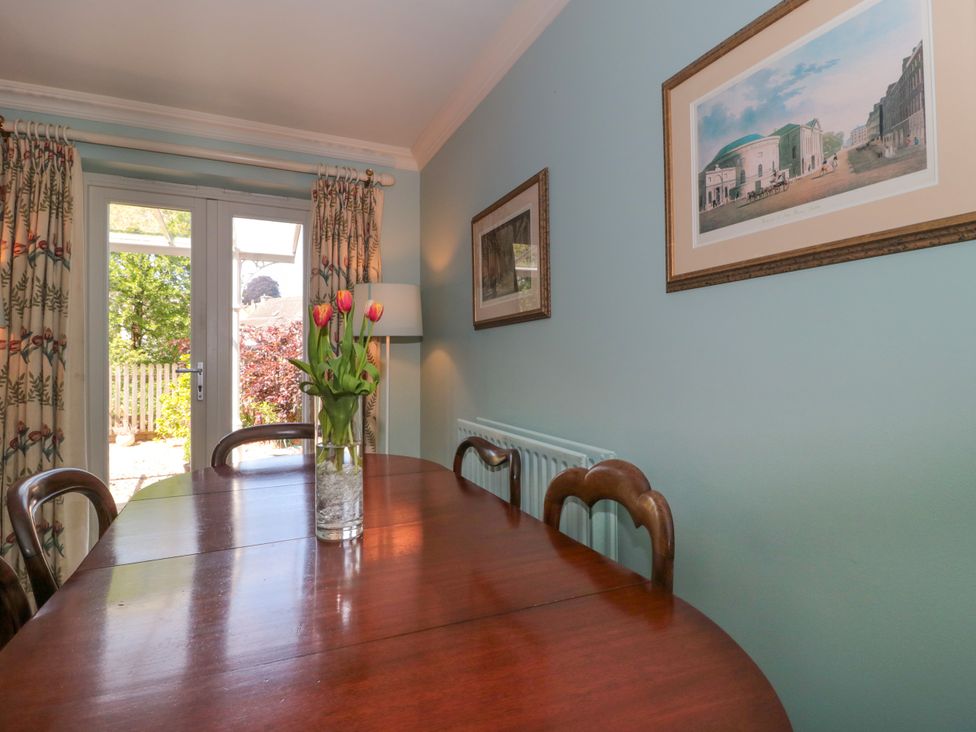 A dining room with a wooden table and chairs with flowers in a vase on the table and framed pictures on the wall at Batemans Nailsworth