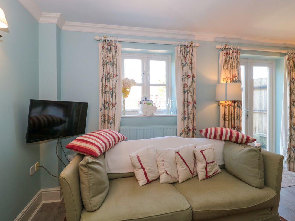 A living room with a green sofa with cushions spelling love a flat screen TV and floral curtains at Batemans Nailsworth
