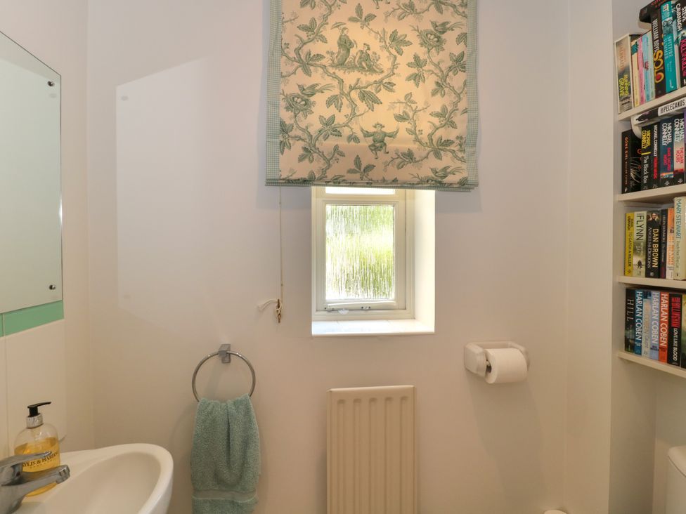 A bathroom with a small window and printed curtain a towel ring with a towel and a wall-mounted bookshelf at Batemans Nailsworth
