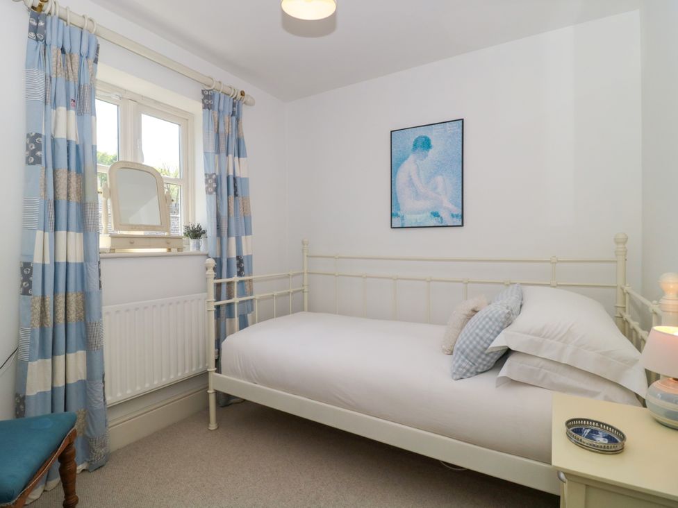 A bedroom with a white metal-framed single bed blue and white curtains and a small table with a lamp and tray at Batemans Nailsworth