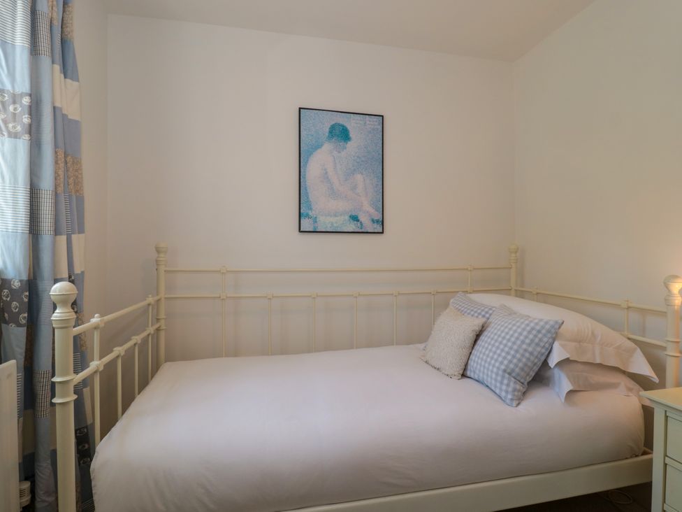 A bedroom with a white metal framed bed pillows a nightstand and a painting on the wall at Batemans in Nailsworth