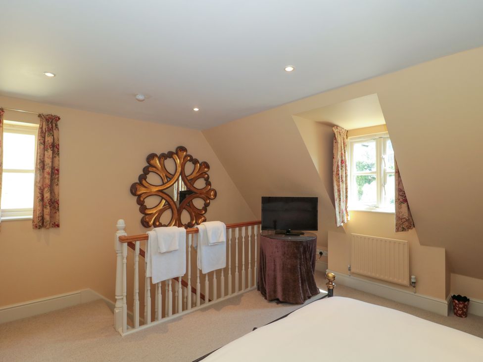 An upstairs bedroom area with a bed railing towels a TV on a covered table and two windows with curtains at Batemans Nailsworth