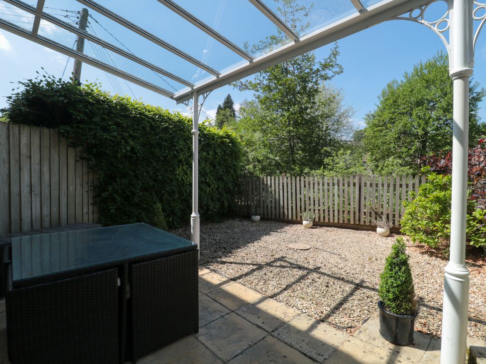 A backyard with a glass canopy a patio table gravel ground and a wooden fence at Batemans Nailsworth