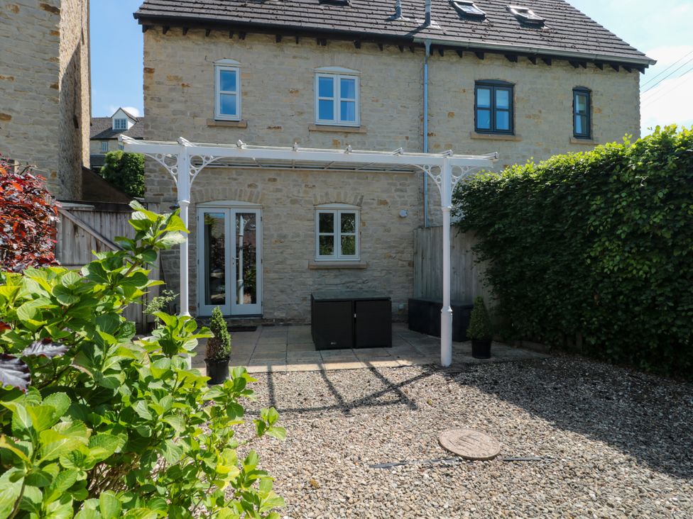 A stone house with white framed windows and doors a white pergola and a gravel and paved garden with plants at Batemans Nailsworth