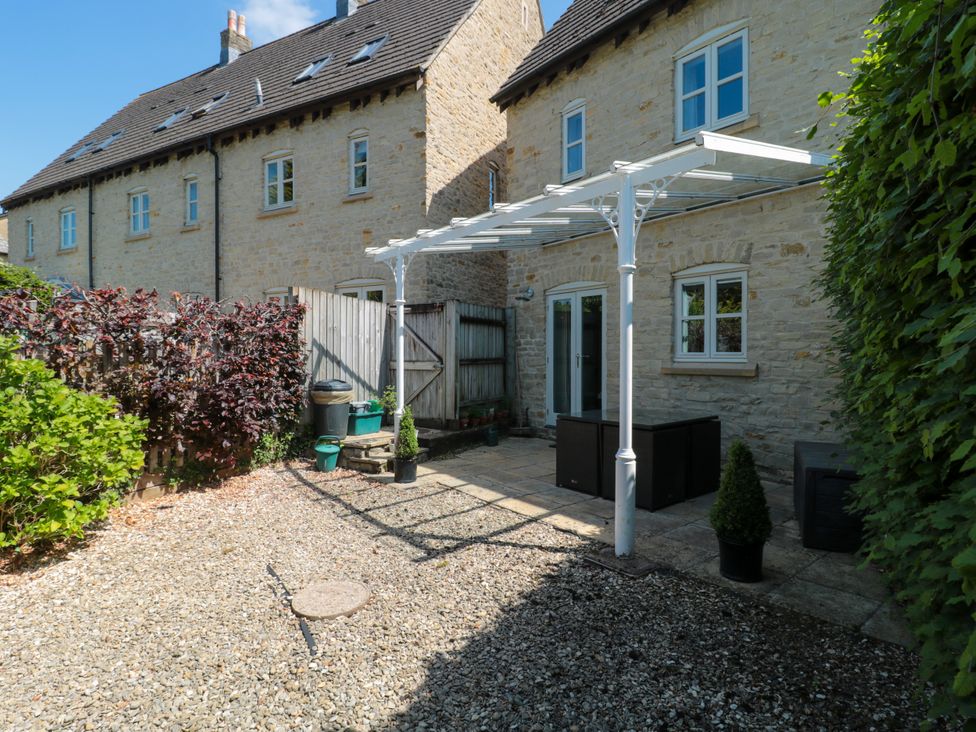 A stone house with a small patio and gravel yard with plants and a white pergola at Batemans in Nailsworth