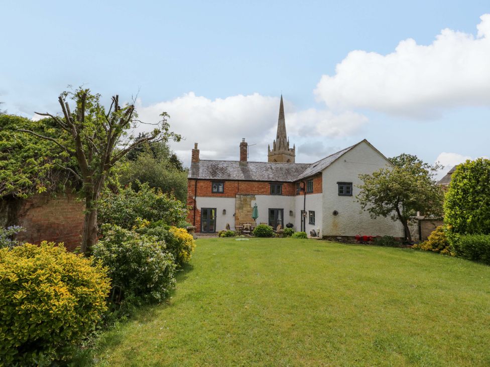 A house with a garden and church in the background at Elmhurst Cottage in Lower Quinton