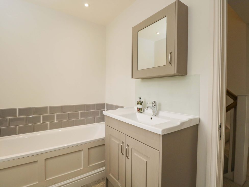 A bathroom with a bath tub, cabinet, and mirror at Church View in Bourton-On-The-Water