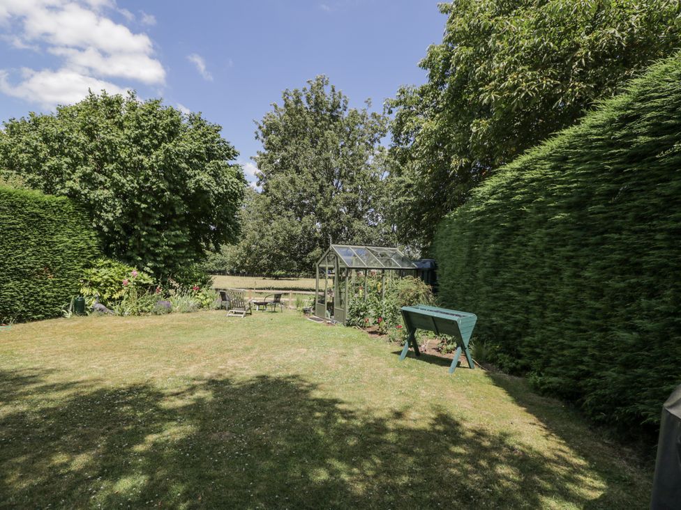 A garden with a greenhouse and seating area at The Old Reading Room Bledington near Stow-on-the-Wold
