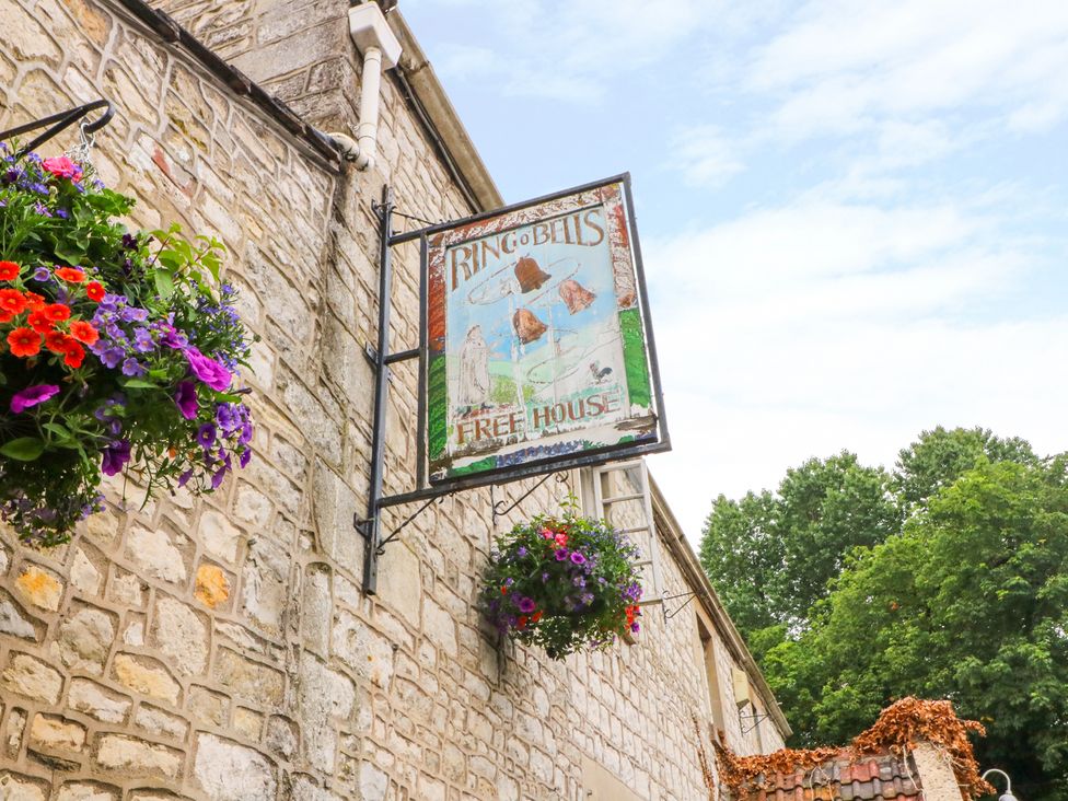 A sign for the Ring O' Bells pub with hanging flowers in Priston Village, Bath