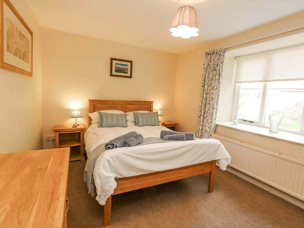 A bedroom with a bed, nightstand, and window at Droop Farm Cottage in Droop near Hazelbury Bryan