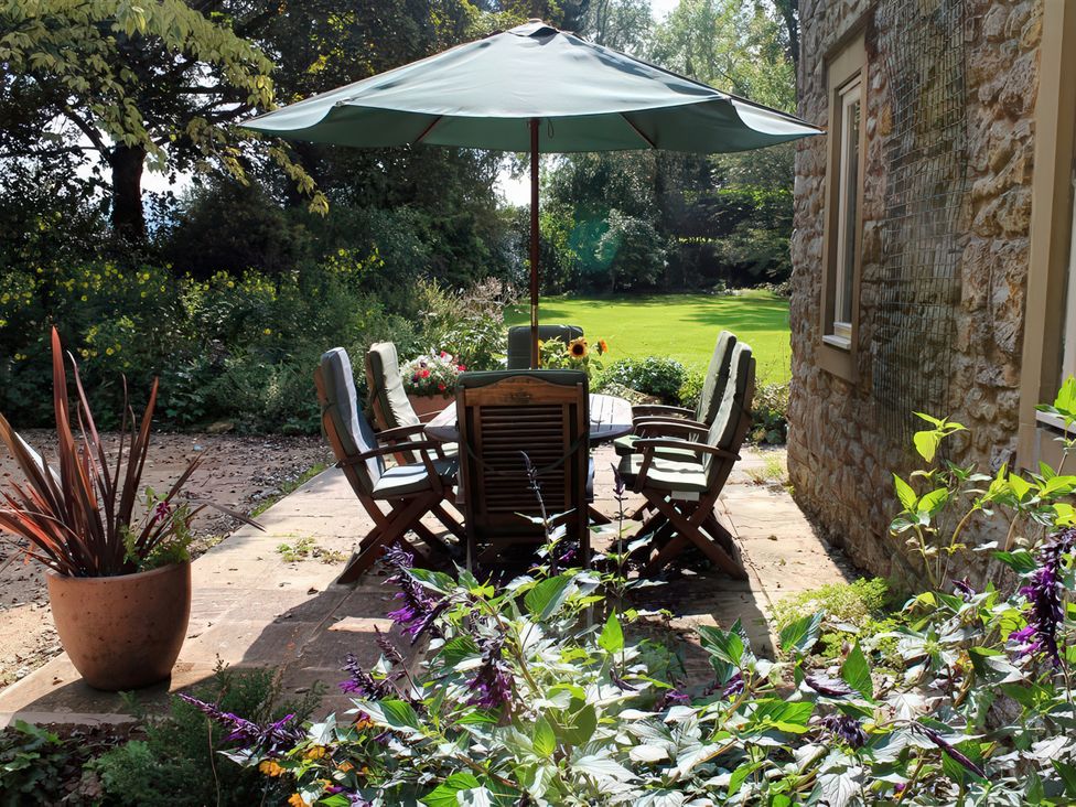 A patio area with a table and chairs under an umbrella at Droop Farm Cottage Droop near Hazelbury Bryan