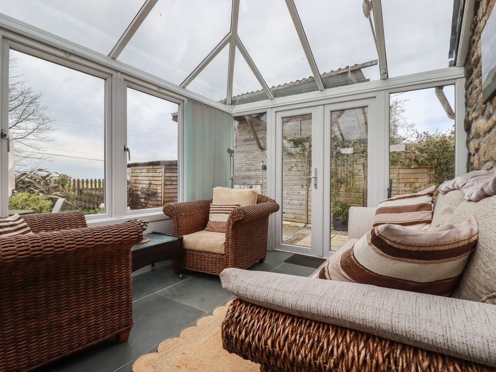 A conservatory with rattan chairs and glass doors at The Smithy in Blisland