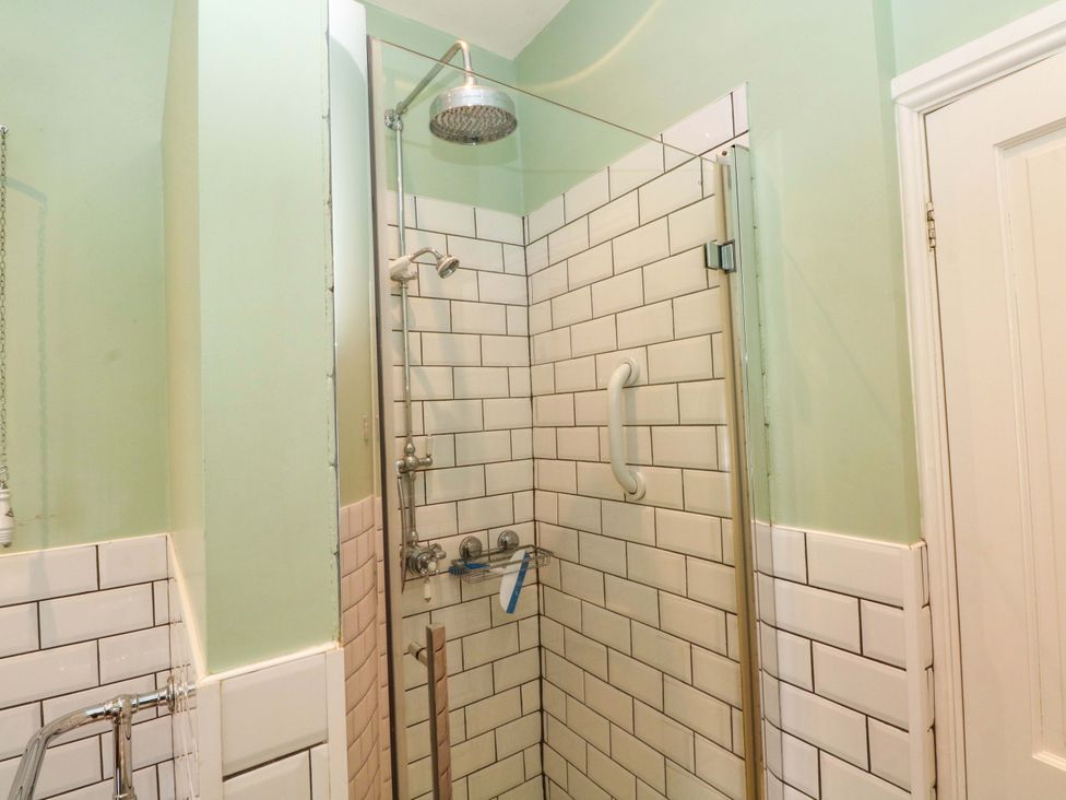 A shower with a glass panel and wall tiles at Sunlight Soap Cottage in Port Sunlight