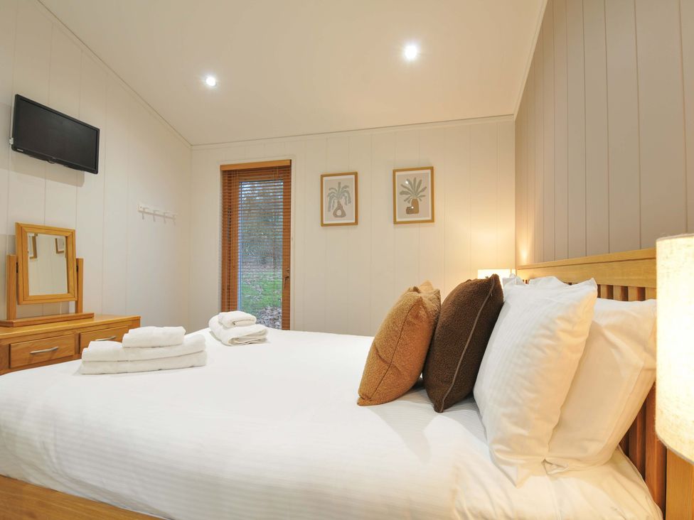 A bedroom with a bed, mirror, TV, and window at 6 Hedgerows in Lanreath