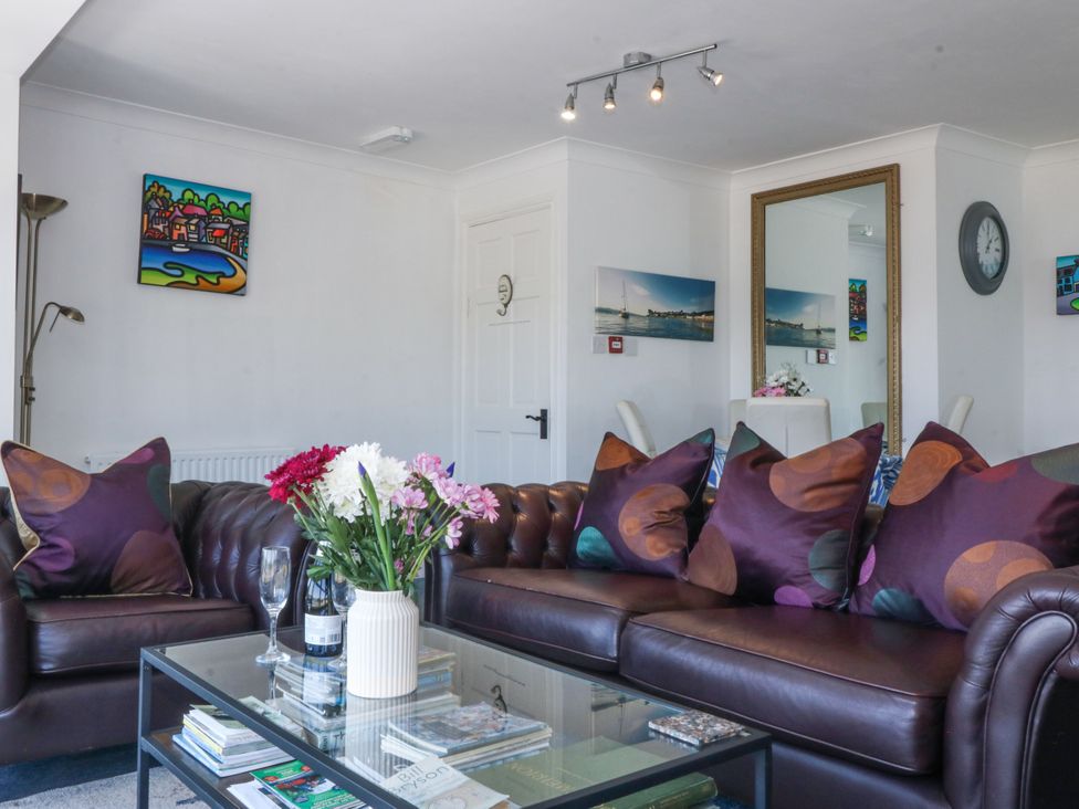 A living room with leather sofas and patterned cushions a glass coffee table with flowers and books a large mirror and wall art at Sea View apartment in Borth-Y-Gest