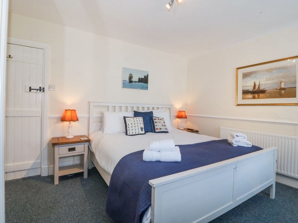 A bedroom with a white bed and blue bedding two bedside tables with lamps and framed pictures on the walls at Sea View apartment in Borth-Y-Gest