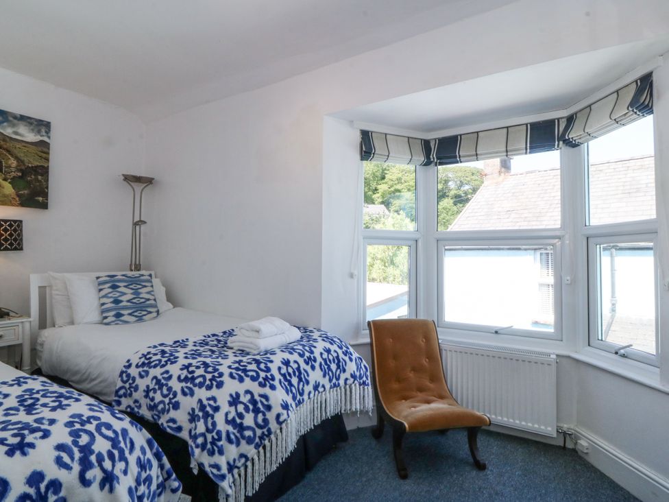 A bedroom with two single beds next to a window and a brown chair near the window in Sea View apartment in Borth-Y-Gest