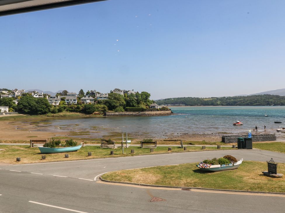 A coastal area with two small boats used as planters on grassy patches near a road by the shoreline with houses and trees in the background at Sea View apartment in Borth-Y-Gest