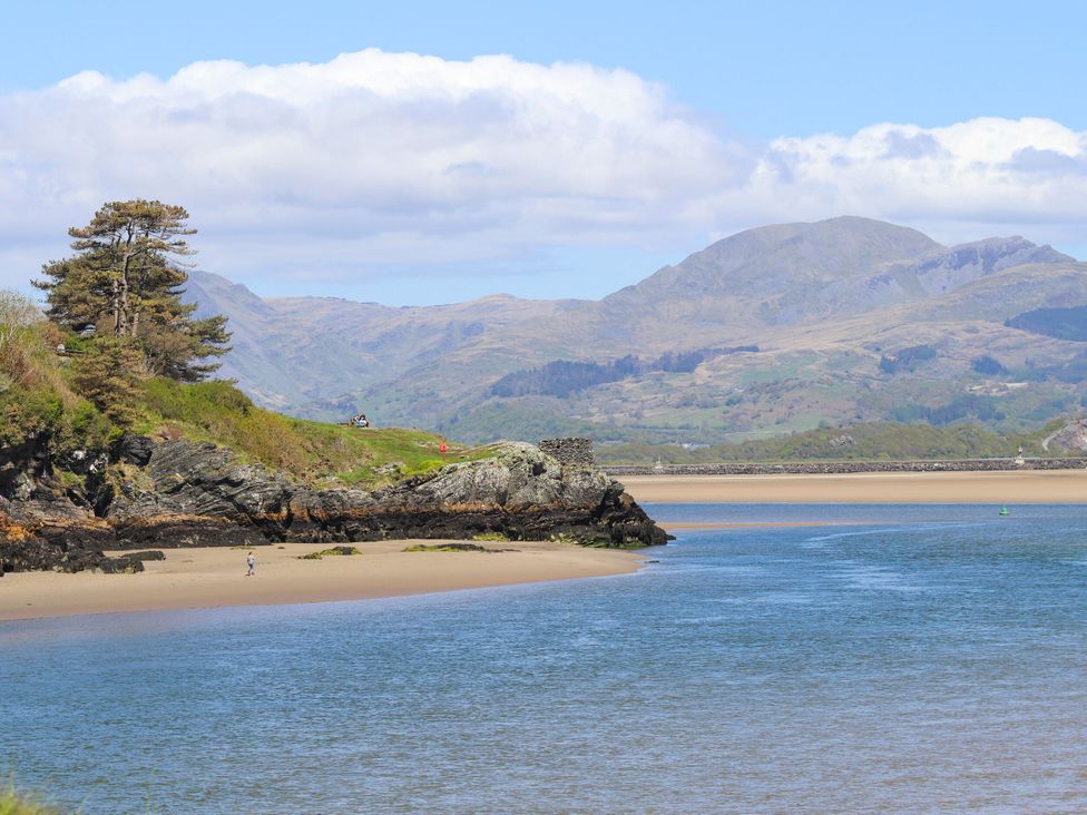 A coastal landscape with a river or inlet flowing into the sea with rocky cliffs and grassy areas and mountains in the background at Sea View apartment in Borth-Y-Gest
