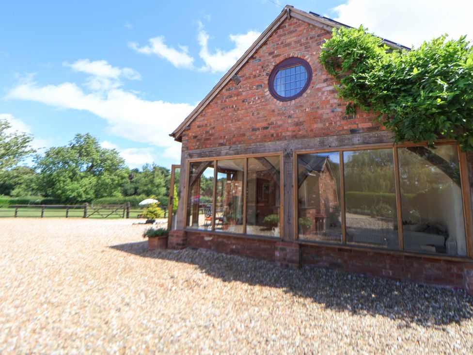 An outdoor view of a brick building with windows and gravel area at Honeysuckle Farmhouse Tarporley