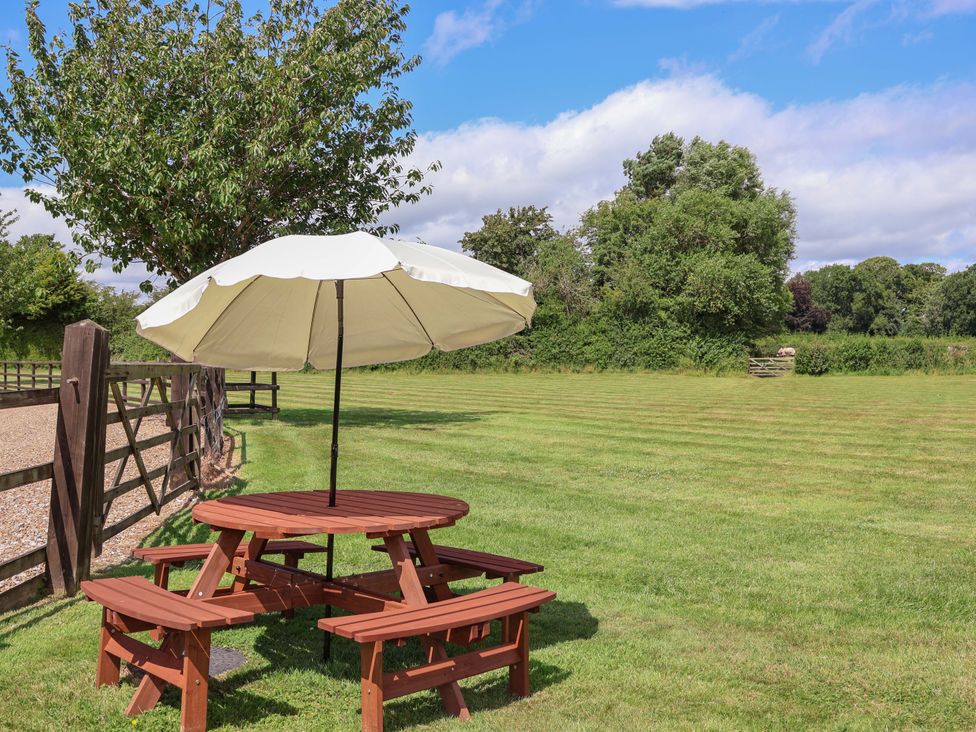 A picnic table with an umbrella in a grass area at Honeysuckle Farmhouse Tarporley