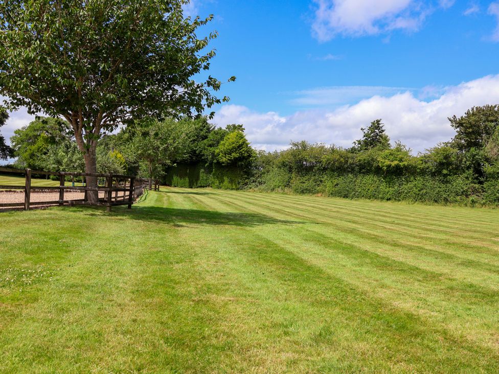 An outdoor view of a lawn with trees and a fence at Honeysuckle Farmhouse in Tarporley