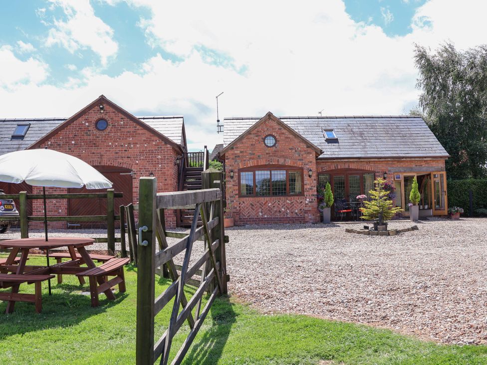 A brick house with a picnic table and a gate at Honeysuckle Farmhouse in Tarporley