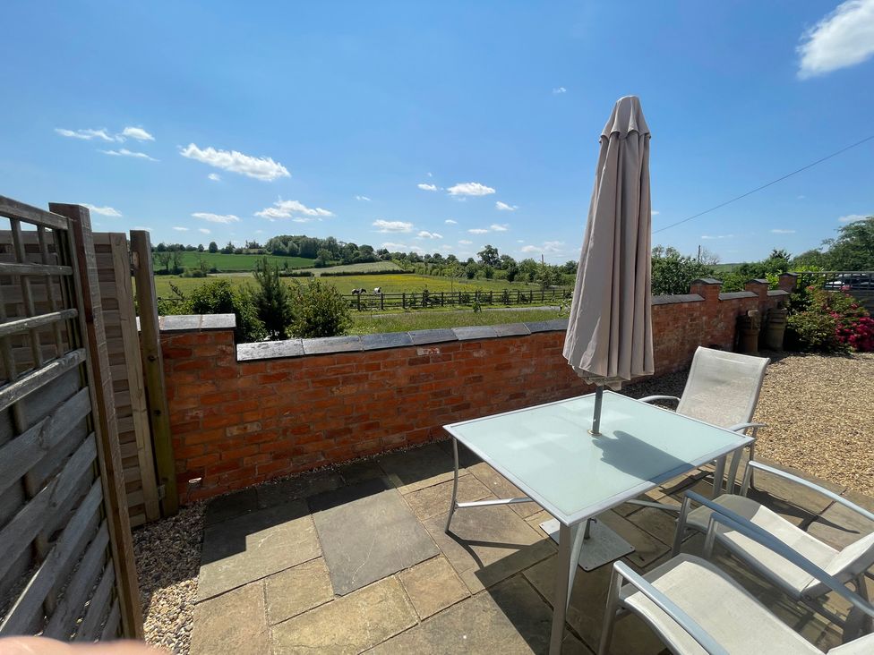 An outdoor patio with a table and chairs and a view of fields at Grooms Cottage Uppingham