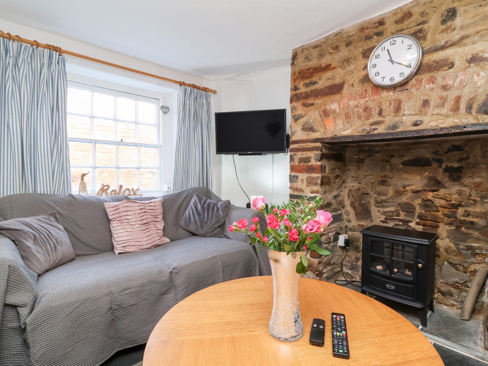 A living room with a sofa, television, and a coffee table at Willets Cottage in Appledore