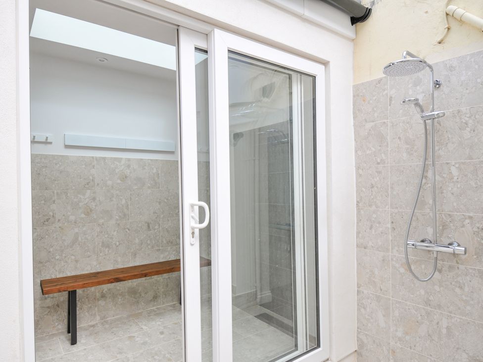A bathroom with a shower and a wooden bench at Cecily Cottage in Westward Ho!