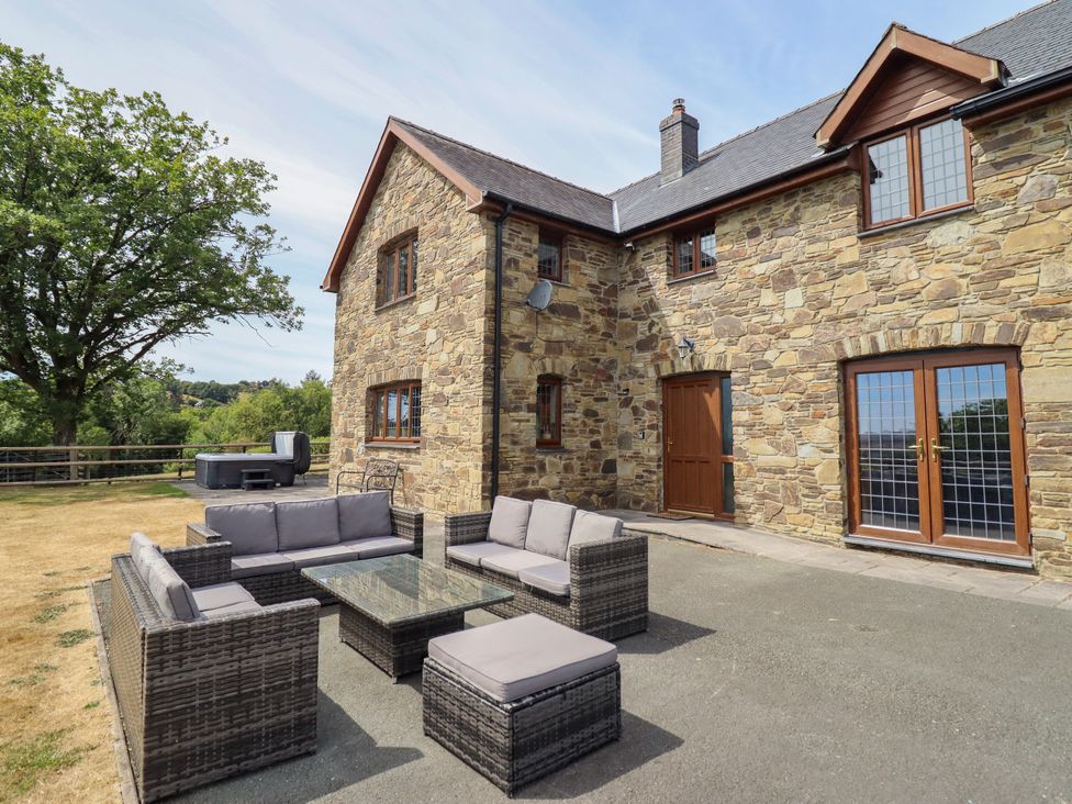 An outdoor seating area with a stone house and hot tub at Ty Berllan Caersws