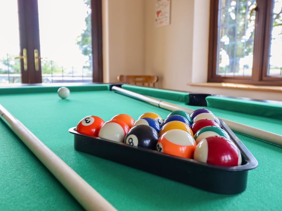 A pool table with balls and cue sticks in a game room at Ty Berllan in Caersws