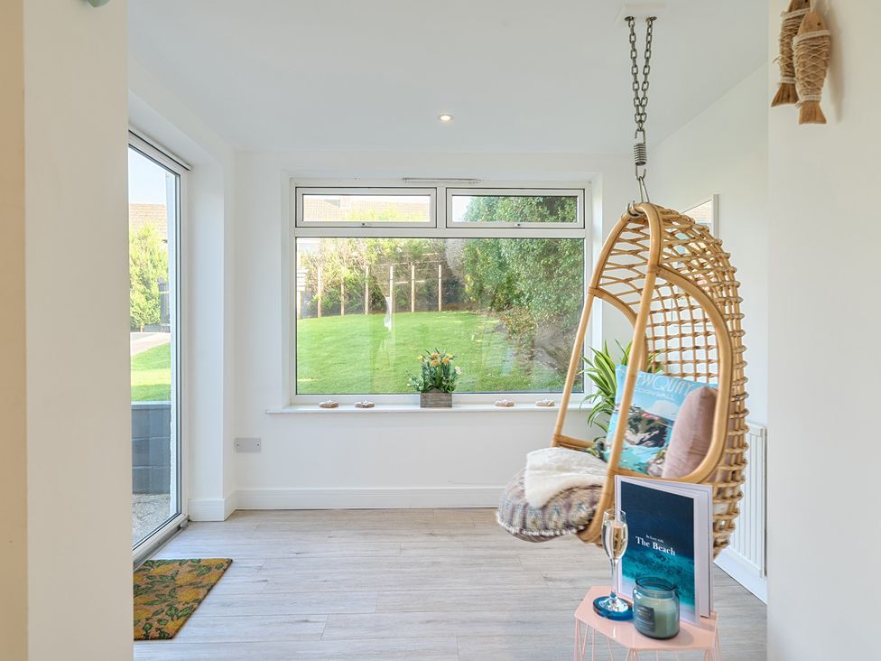 A snug with a hanging chair and window overlooking the garden at Chi An Mor in Porth