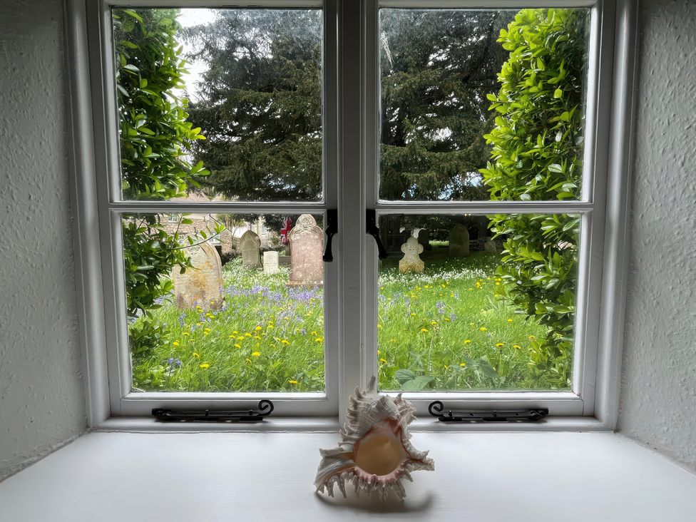 A window view of a graveyard with a shell on the sill at Ivy Cottage in West Lulworth