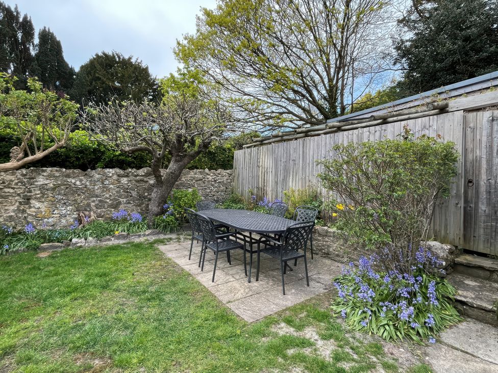 A garden with a table and chairs surrounded by trees and flowers at Ivy Cottage in West Lulworth