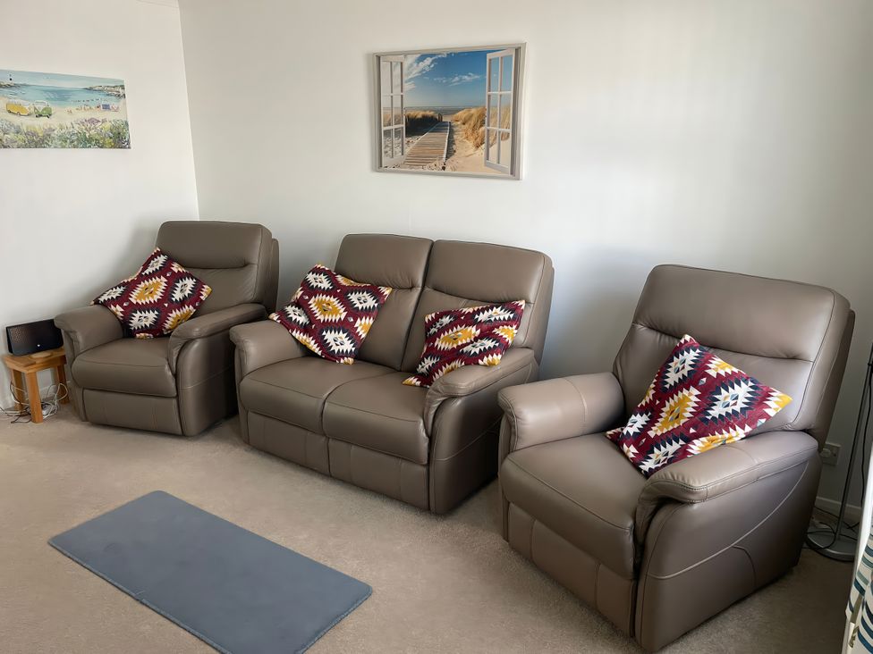 A living room with three leather sofas and a painting at Maisy Cottage in Weymouth