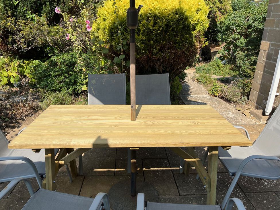 A table with chairs and an umbrella in a garden at Pebbles Burton Bradstock