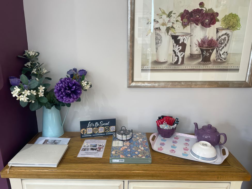 A table with flowers, books, a teapot, and a picture at Pedaller's Cottage in Weymouth