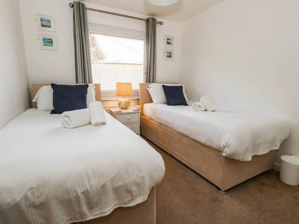Two single beds in a bedroom with curtains and a lamp at Tides Corner Bowleaze