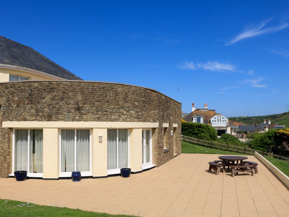 A stone and stucco house with large windows and a patio with a round wooden table and benches at 2 Sea Gardens in Hope Cove