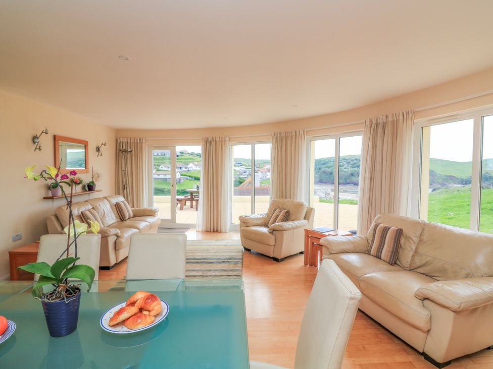 A living room with beige leather sofas and large windows overlooking a green landscape at 2 Sea Gardens in Hope Cove