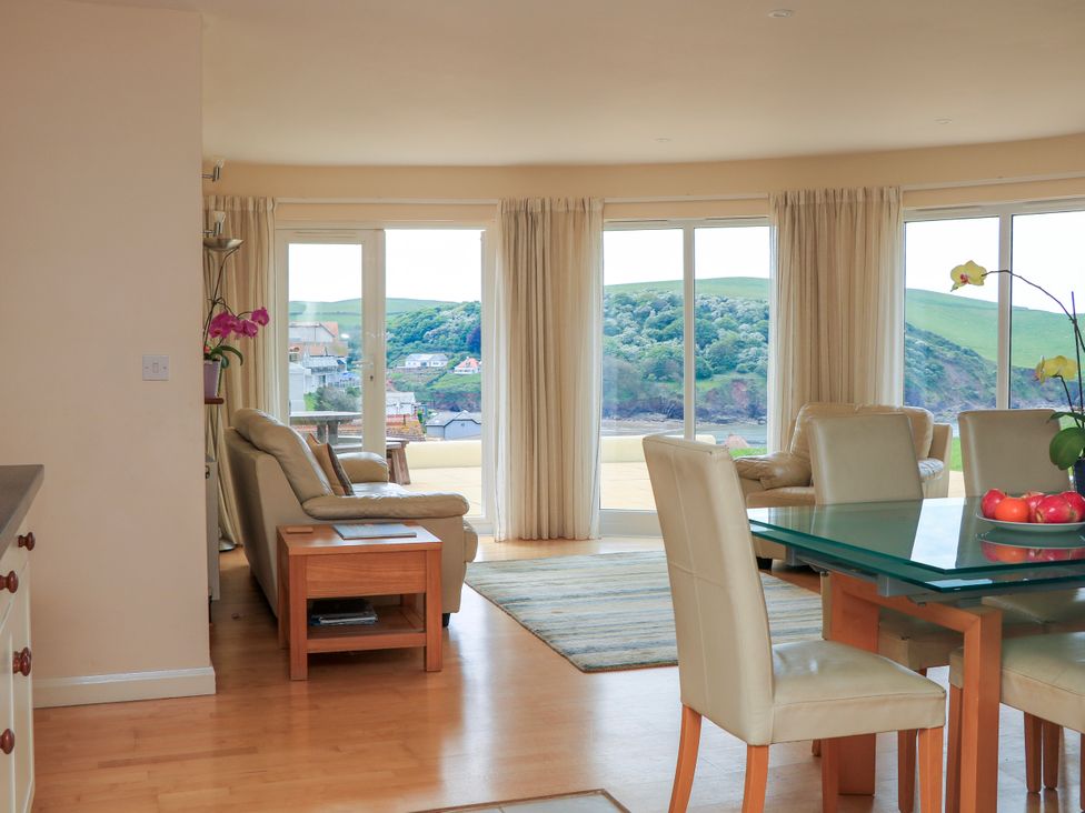 A living room with leather sofas glass dining table and large windows showing hills at 2 Sea Gardens in Hope Cove