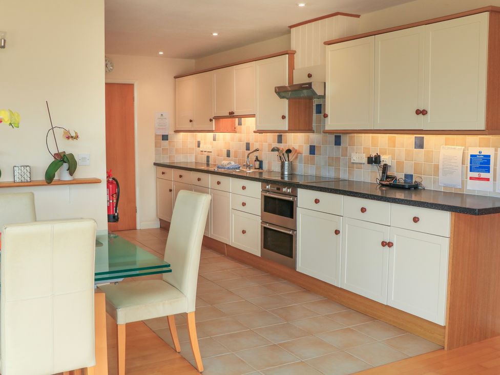 A kitchen with cream cabinets tiled backsplash glass dining table and cream chairs at 2 Sea Gardens in Hope Cove