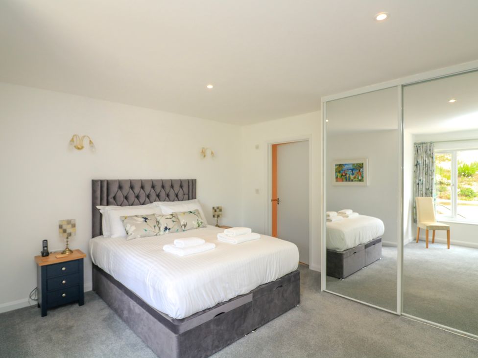 A bedroom with a bed bedside tables a chair a large mirrored wardrobe and a window at 2 Sea Gardens Hope Cove