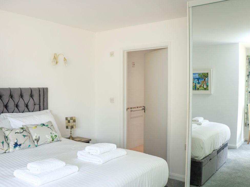 A bedroom with a made bed with pillows and towels with a bedside table and lamp at 2 Sea Gardens in Hope Cove