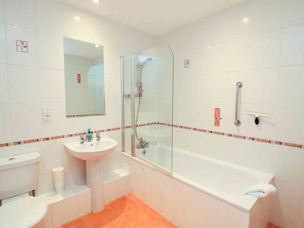 A bathroom with a toilet, pedestal sink, bathtub with a shower and glass screen at 2 Sea Gardens in Hope Cove