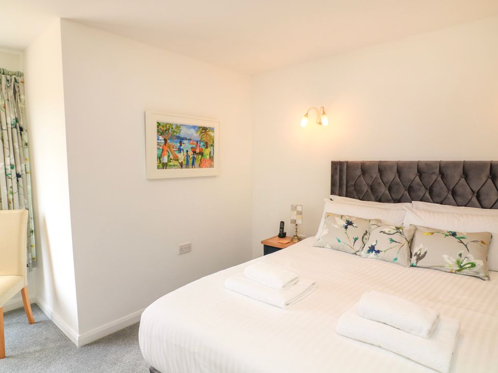 A bedroom with a bed with pillows and towels a bedside table with a lamp and phone a chair and a painting on the wall at 2 Sea Gardens in Hope Cove
