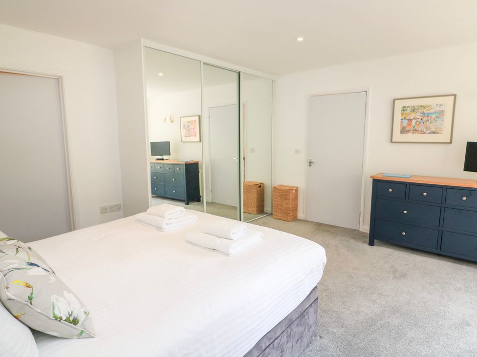 A bedroom with a bed with folded towels a blue dresser with a small TV a wicker basket and a large mirrored closet door at 2 Sea Gardens in Hope Cove