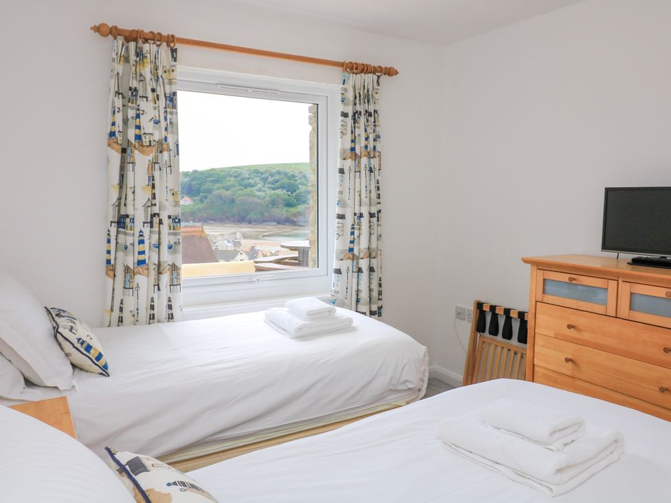 A bedroom with two single beds a wooden dresser and a window with curtains showing a view of a hillside at 2 Sea Gardens in Hope Cove